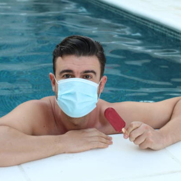 Man wearing surgical mask in the pool holding ice cream.
