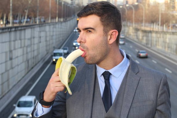 Elegant man biting a banana.