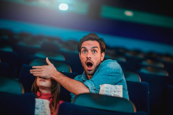 Father and daughter at the cinema watching a movie, eating popcorn