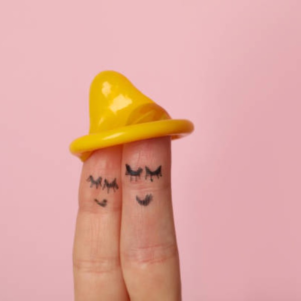 Two fingers with satisfy faces and condom on pink background